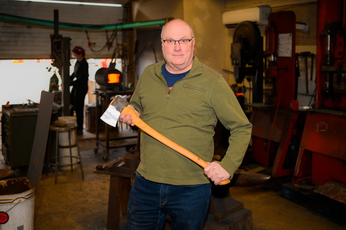 Mark Ferguson holding an axe, with a worker in the background, at the factory.