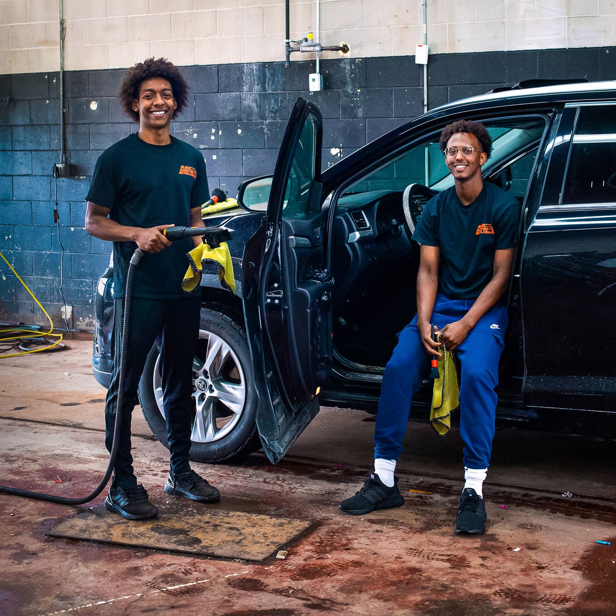 Owners of Black Diamond Detailing inside garage with car.