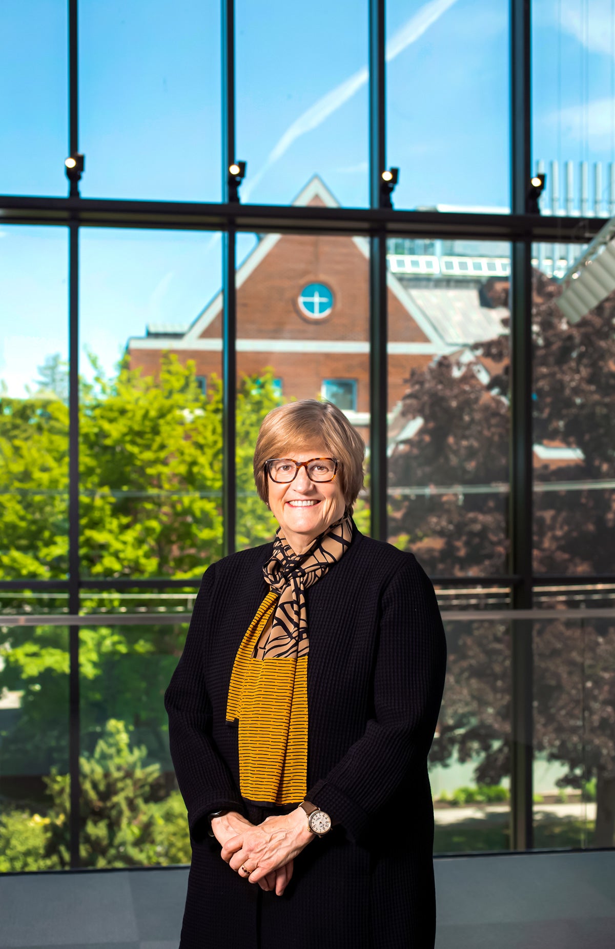 woman with short blonde hair and glasses standing in front of window