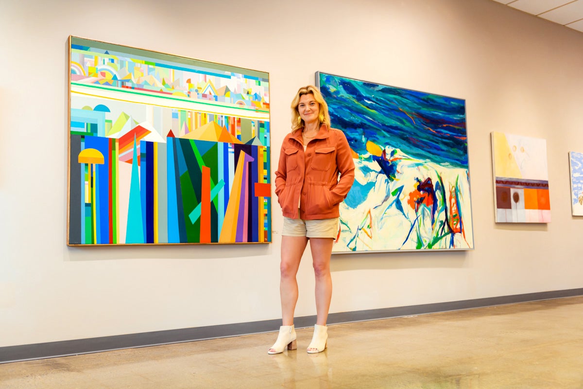Elizabeth Moss standing in front of paintings in her Falmouth gallery