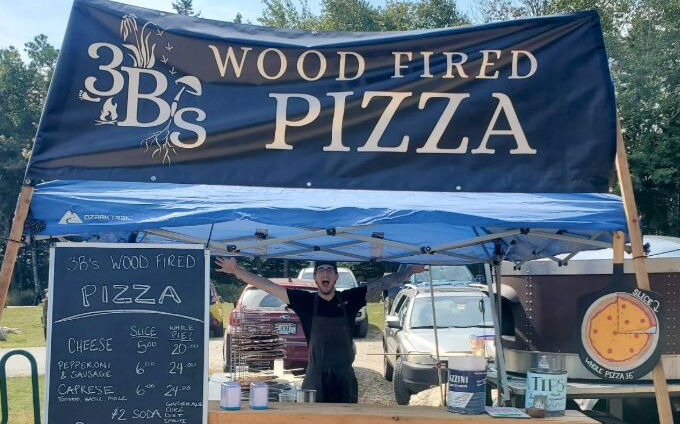 A person stands at a booth with a banner overhead.