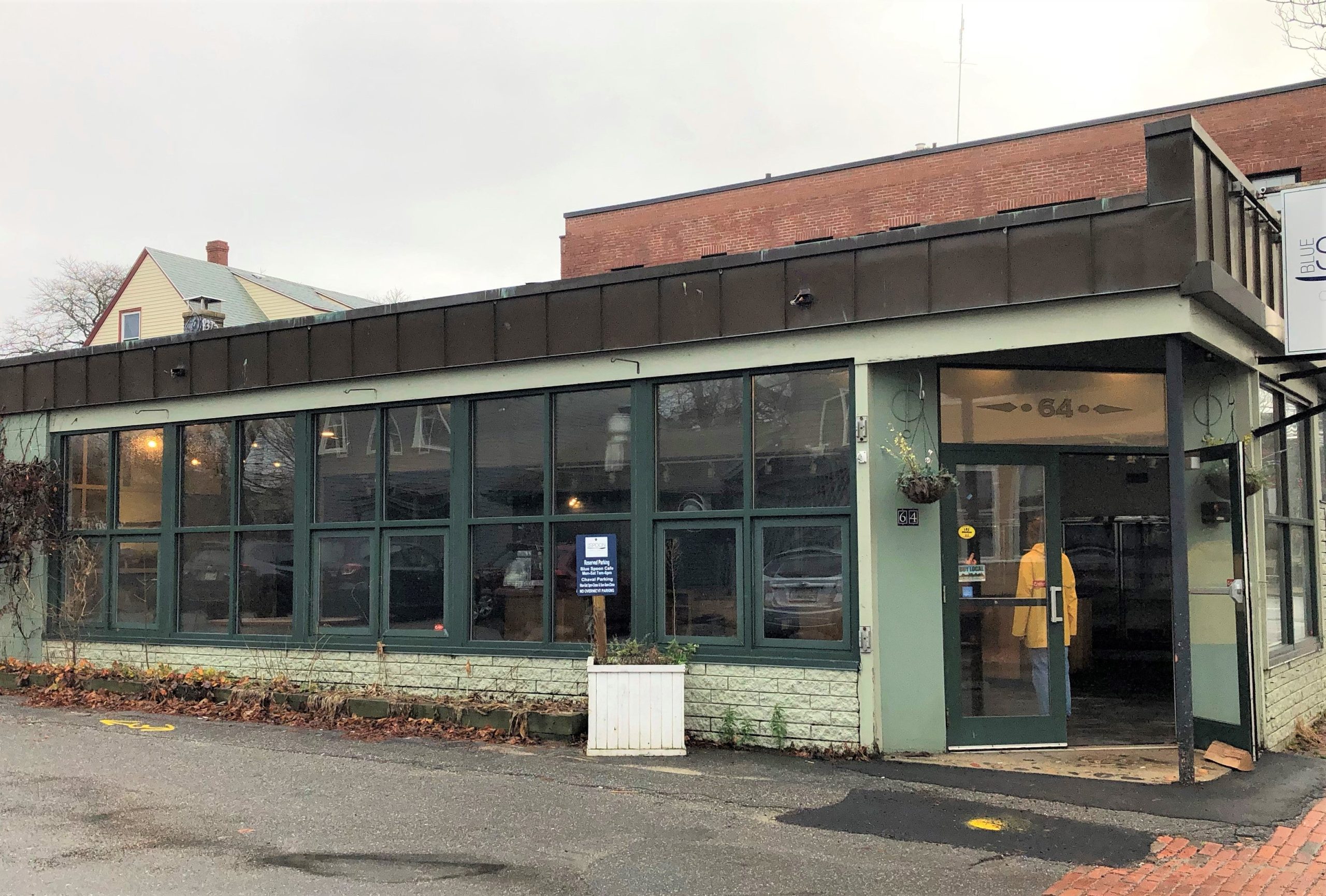 a one story building with a wall of windows a woman in a yellow raincoat stands in the doorway