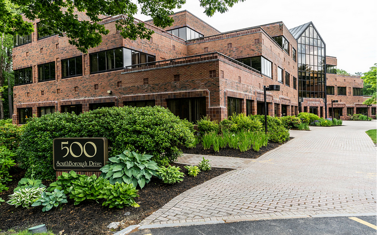 A building has multiple levels, a sign and bushes.