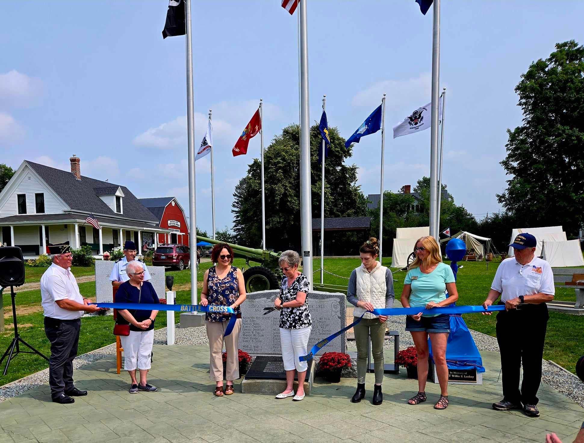 People gather at monument and cut a ribbon.