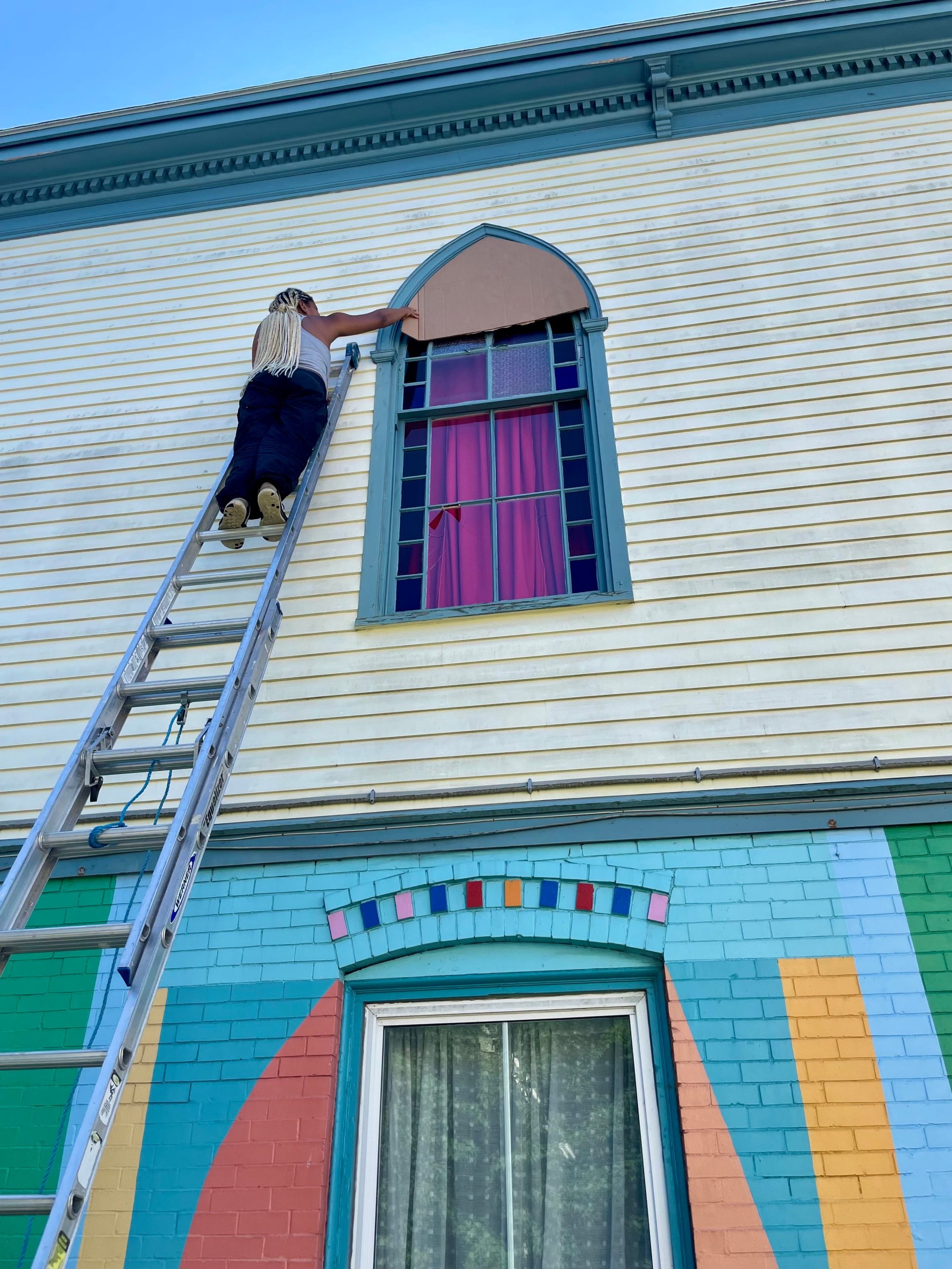A person is on a ladder outside of Mayo Street Arts.