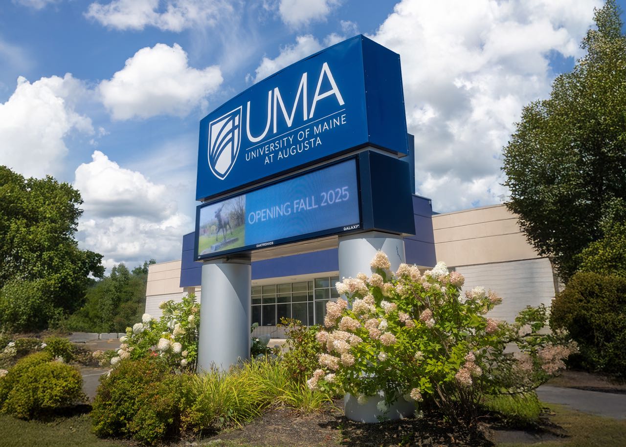 A building with a sign and flowering bushes.