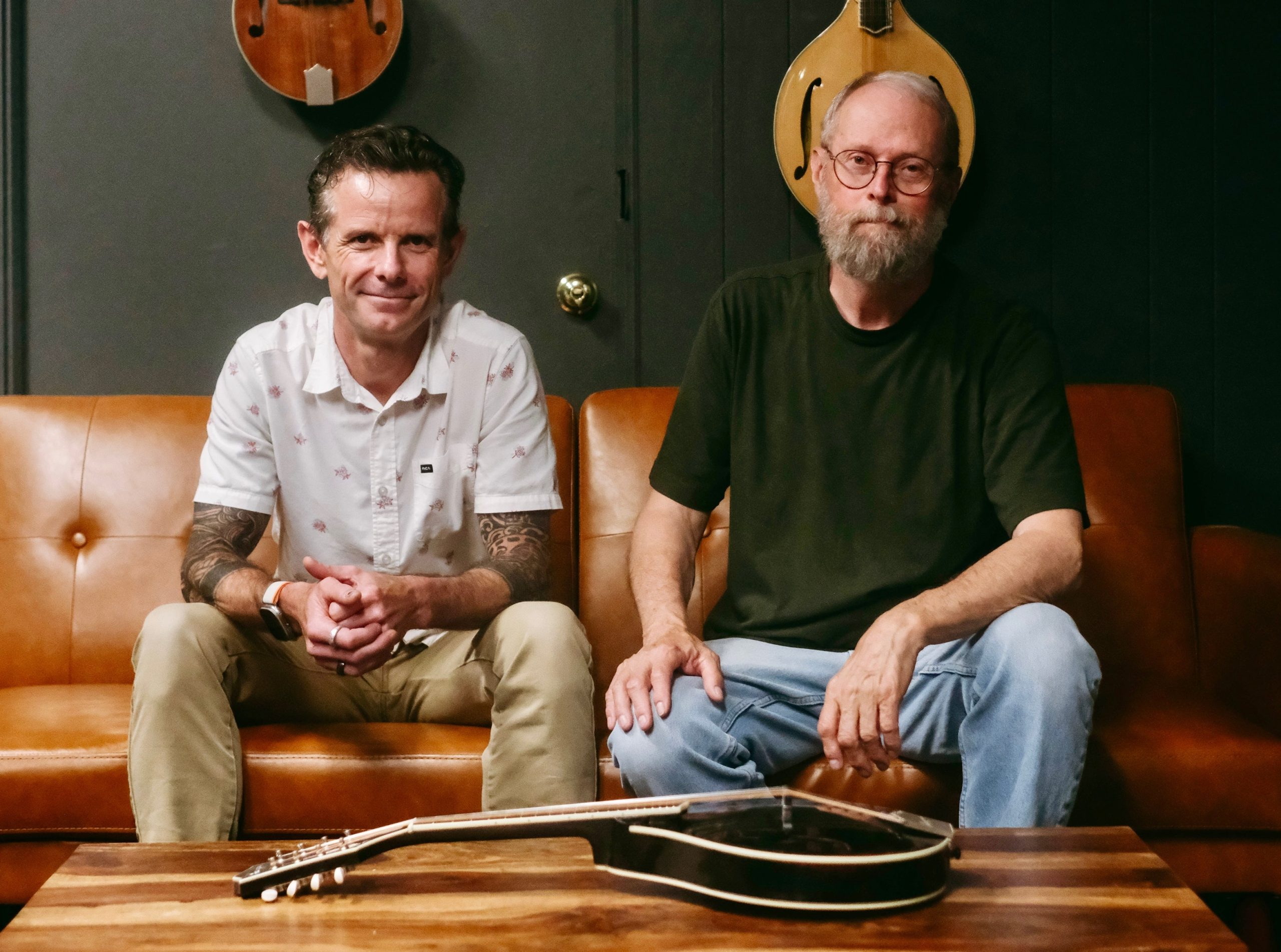 Two people with Bourgeois Guitars sit on a couch with a mandolin in front of them.