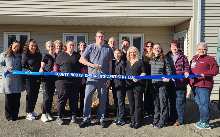 A group of people gather outside a building to cut a ribbon.