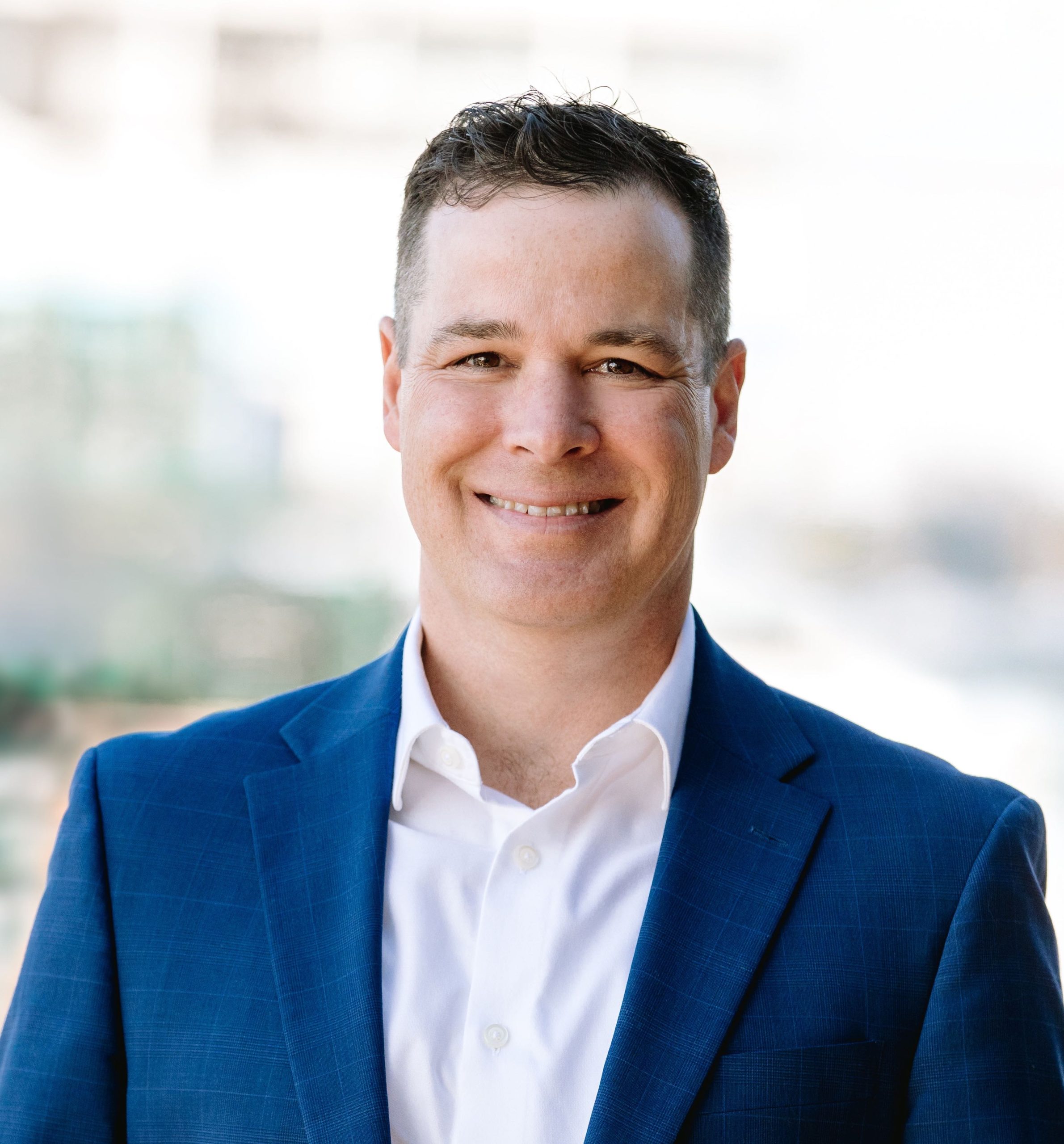 A headshot of a person in a blue blazer and white button-down.
