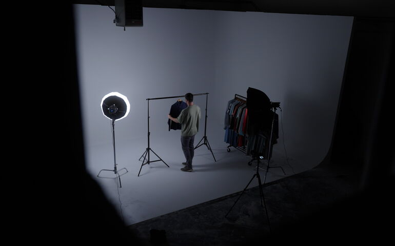 An upper viewa shows a person setting up clothes on a rack against a backdrop.