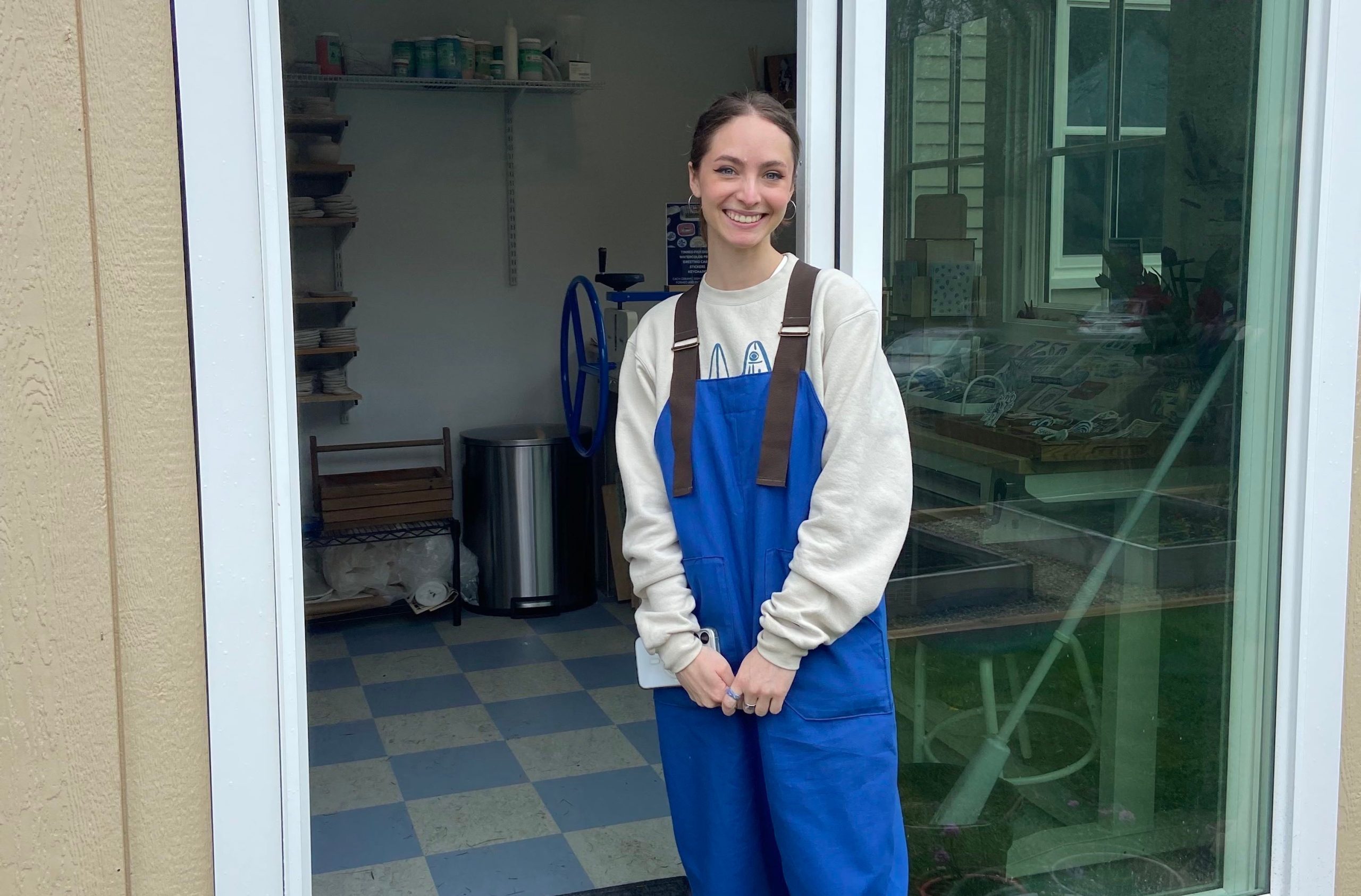 A person in overalls stands outside a door.