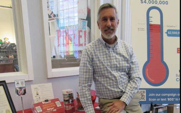 Ed Gardner sits on a table in an office.