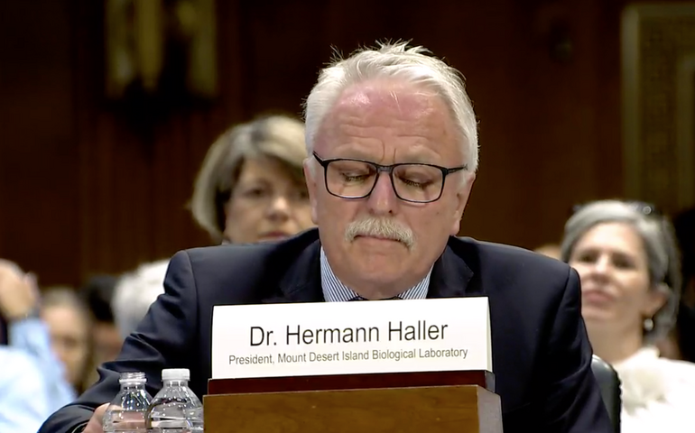 A person sits at a table with other people behind him.