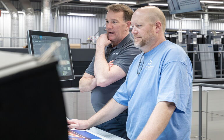 Two people look at a computer setup with machinery off to their side.