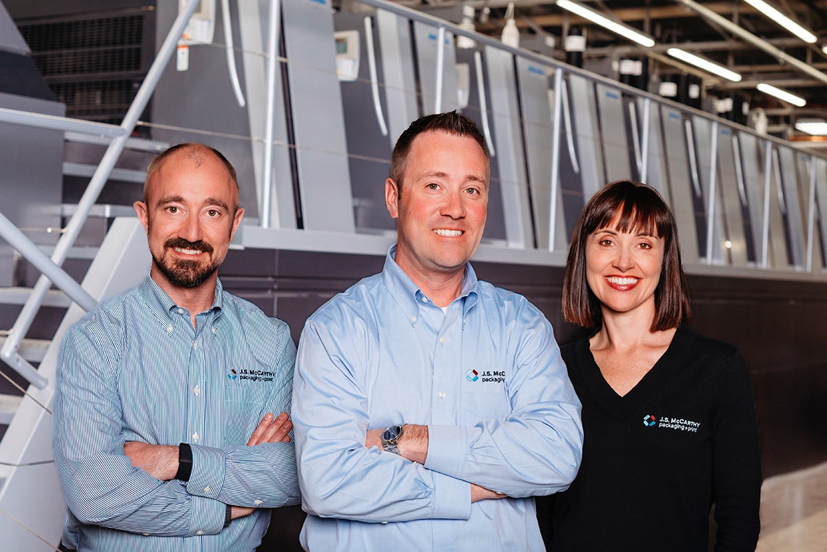 Three people in front of industrial machinery.