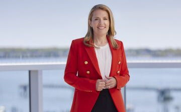 Melissa Smith stands on a deck and wears a red blazer.