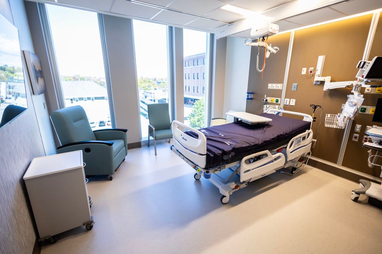 A room has a hospital bed and chars and medical equipment plus windows.