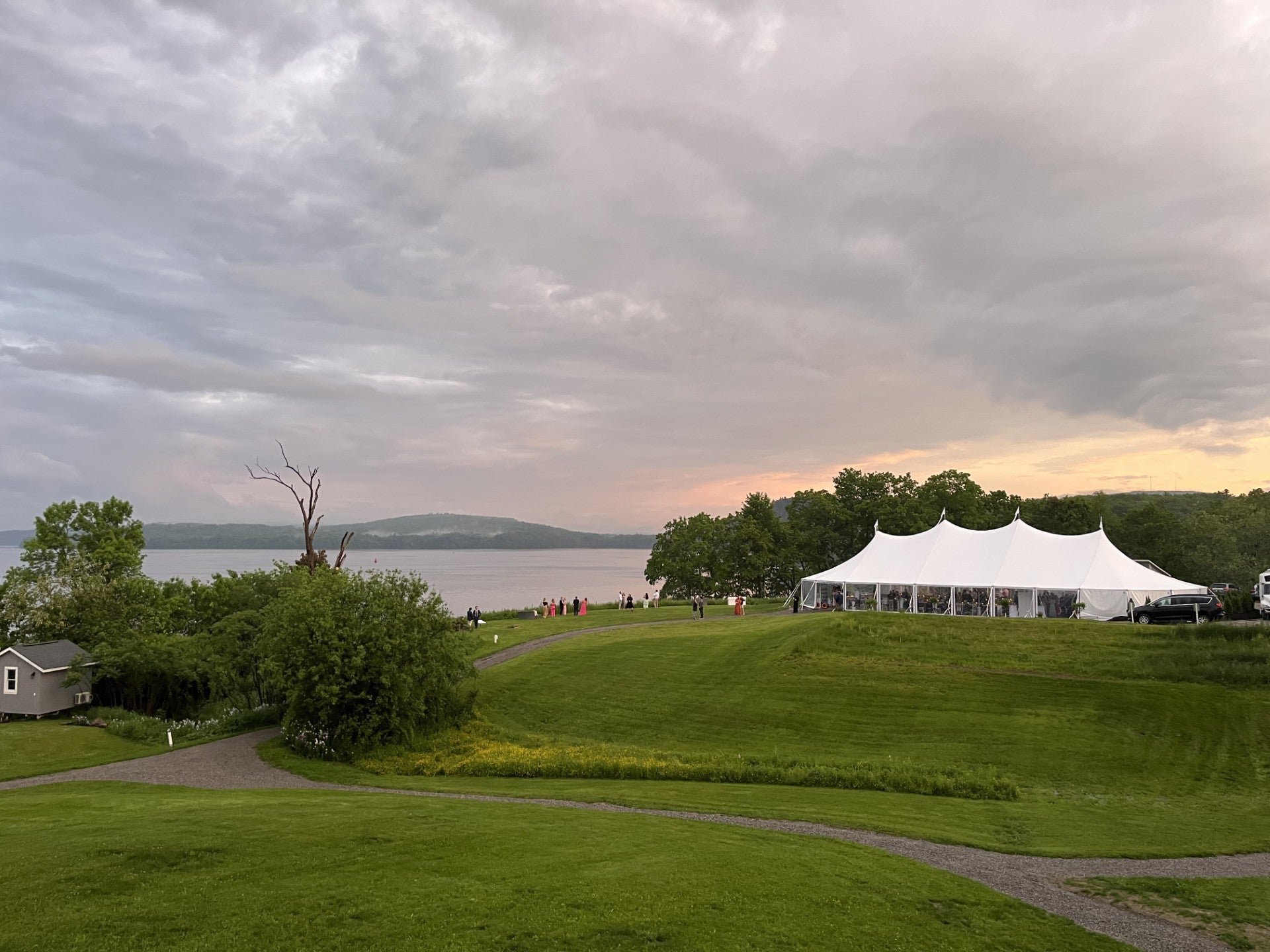 A white tent sits near the water in a field.