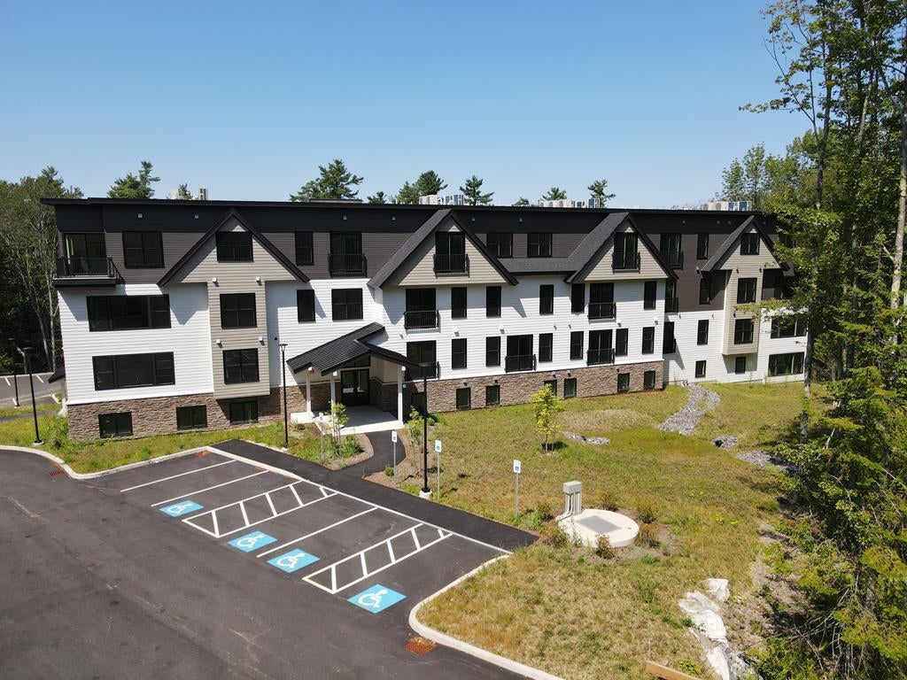 An aerial photos shows a building with white siding and a lawn and parking lot.