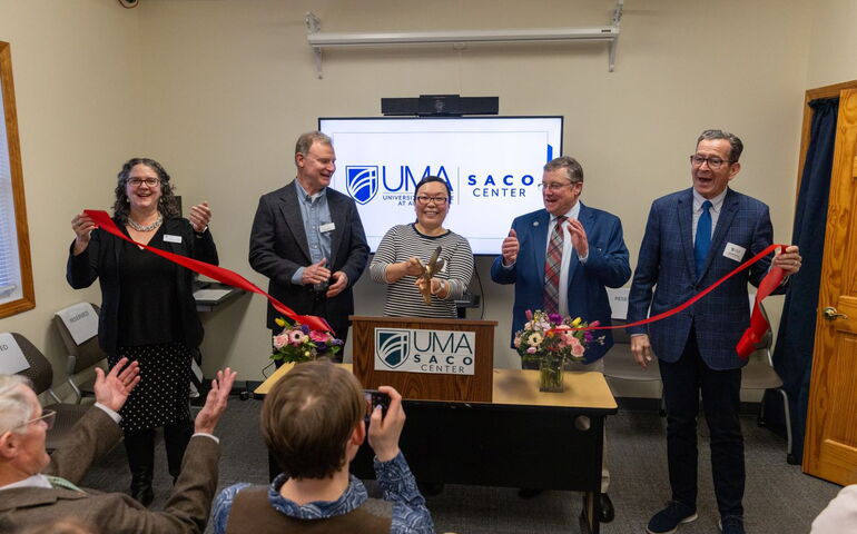 Five people pose in a line with a red ribbon.