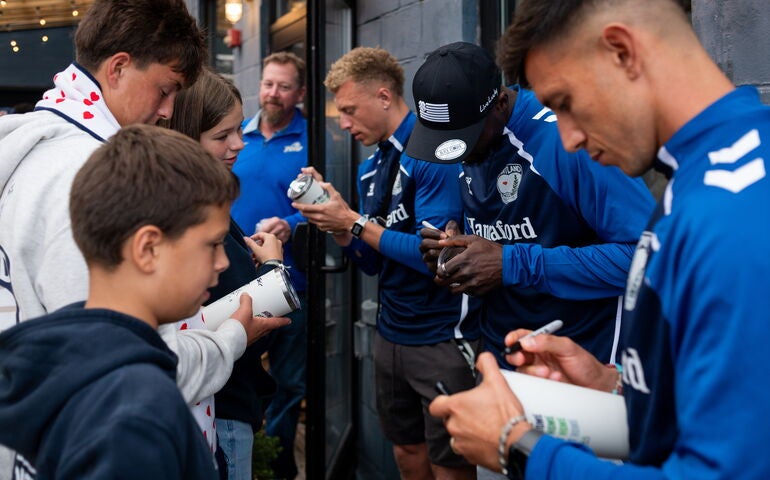 People in blue jackets are signing things while others look on.