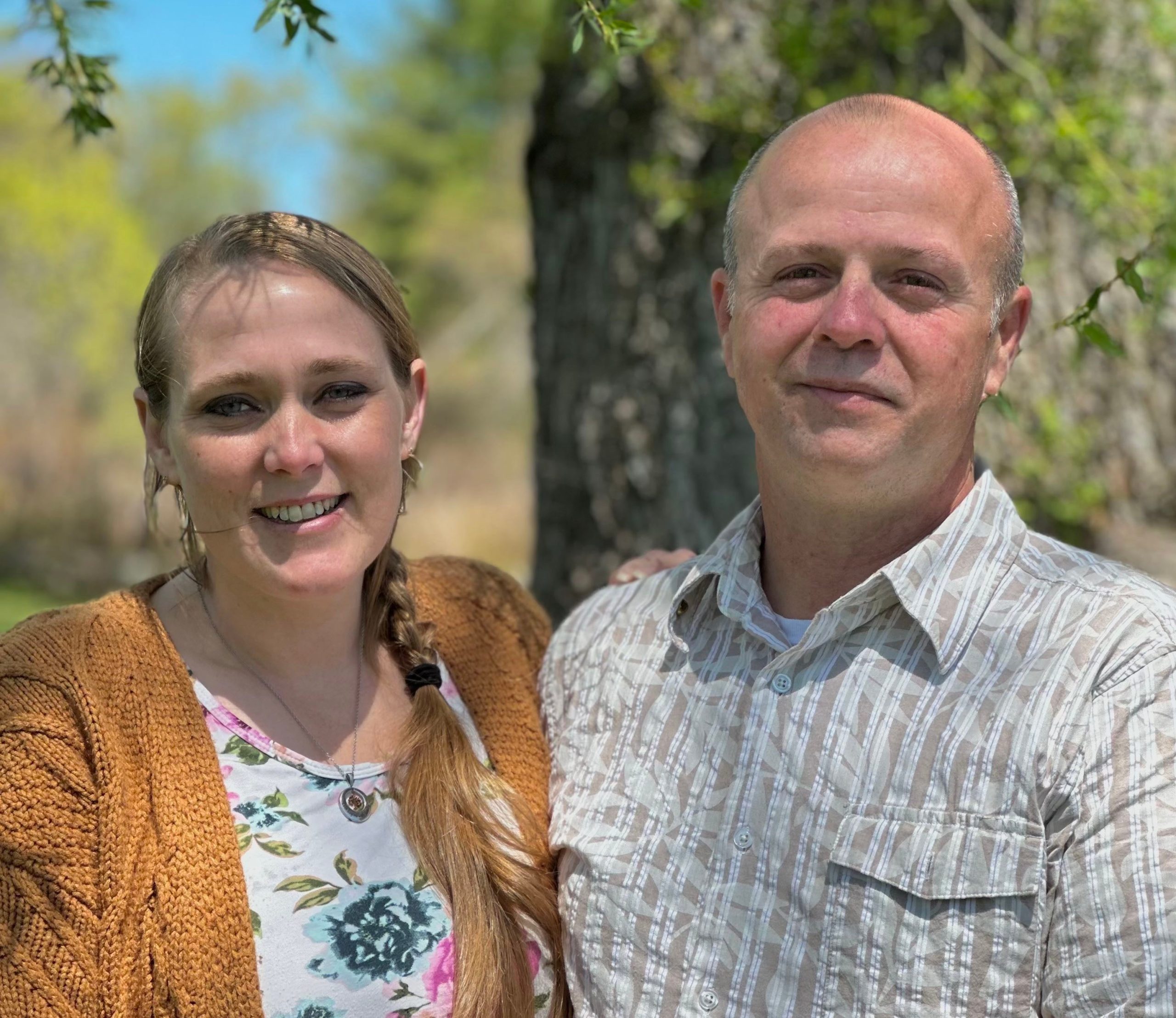 Two people pose near a tree.