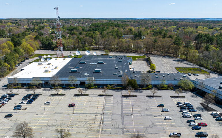 An aerial view of a long low building and parking lot.
