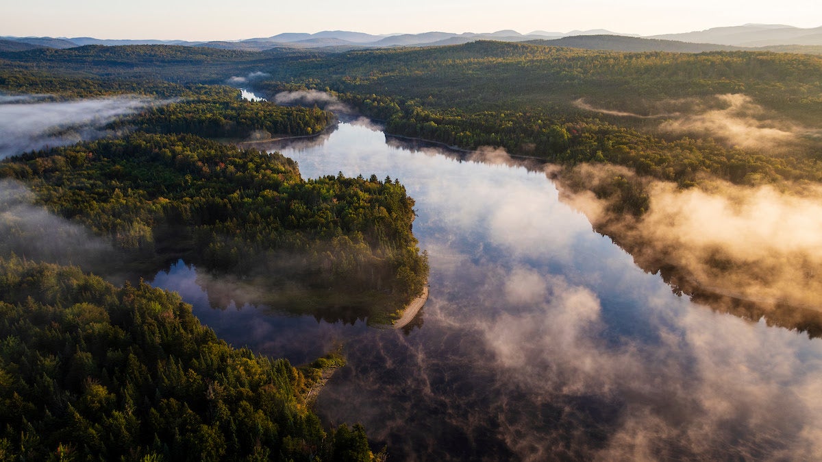 An aerial view shows a river and woods.