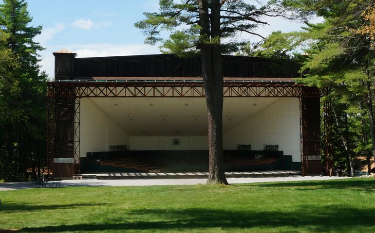 an outdoor shell-style stage with slight art deco features and a large lawn and surrounded by pine trees