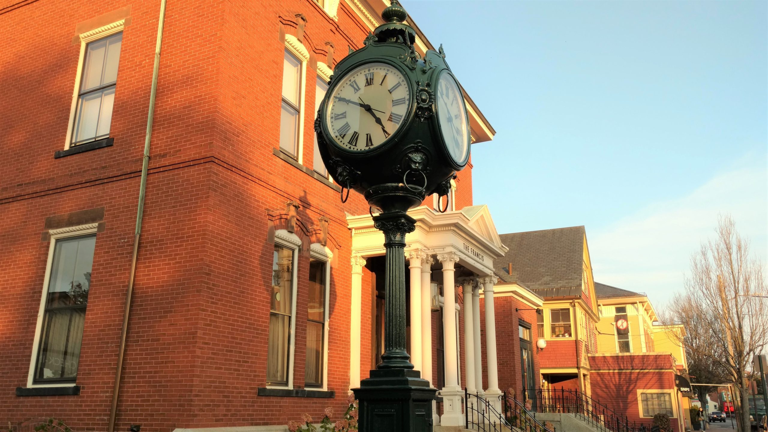 historic outdoor clock on street, in front of red brick victorian house