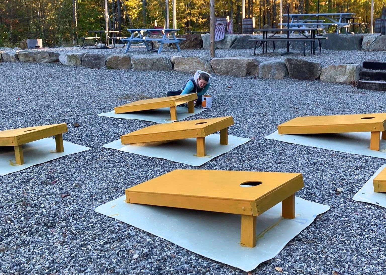 A person paints wooden objects outside.