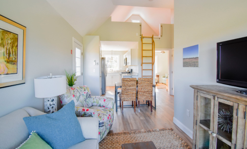 A bright living space that goes back to a kitchen, with white walls and sun coming in the windows
