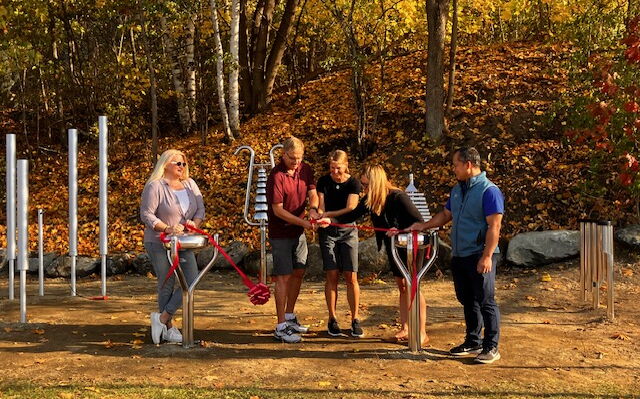 Five people cut a ribbon in front of big musical instruments.