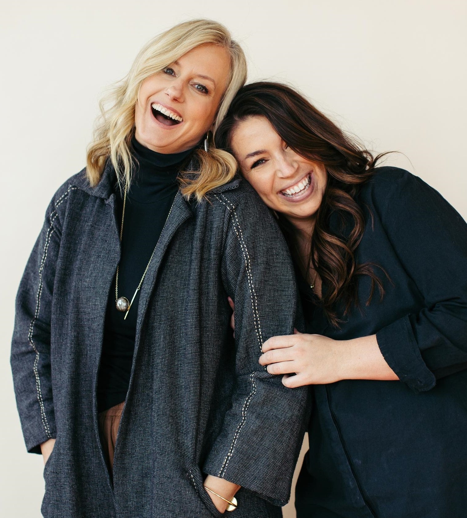 Two white women leaning on each other and laughing, one blond and one brunette