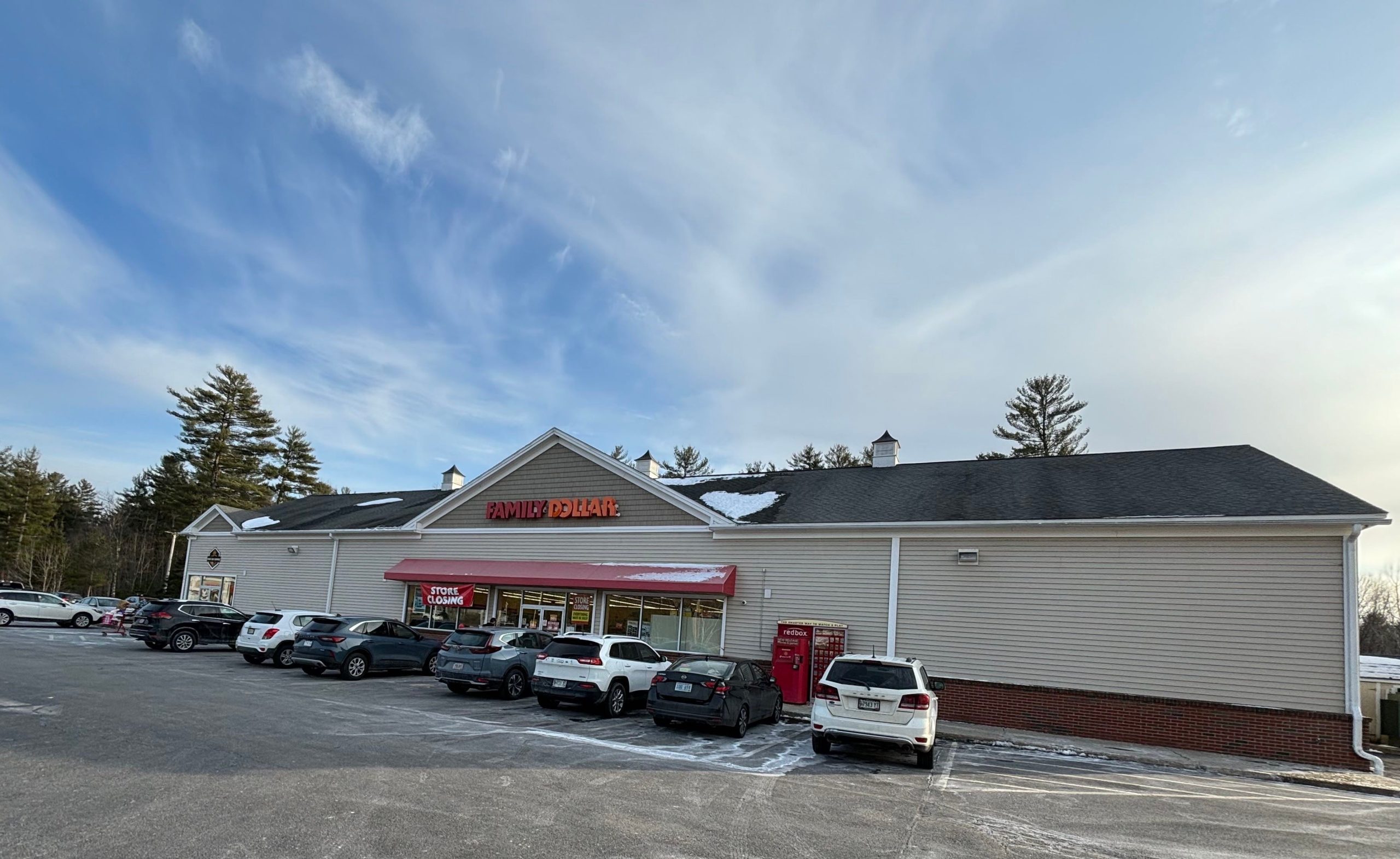 An exterior view of a tan-sided store with cars out front.