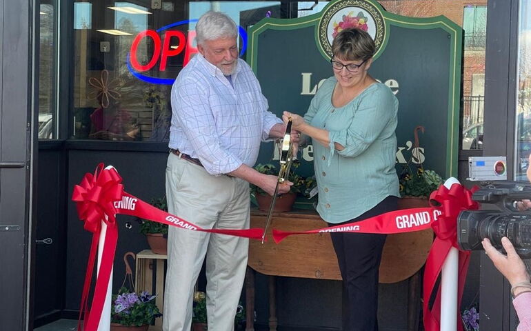 Two people pose with oversize scissors and a ribbon.