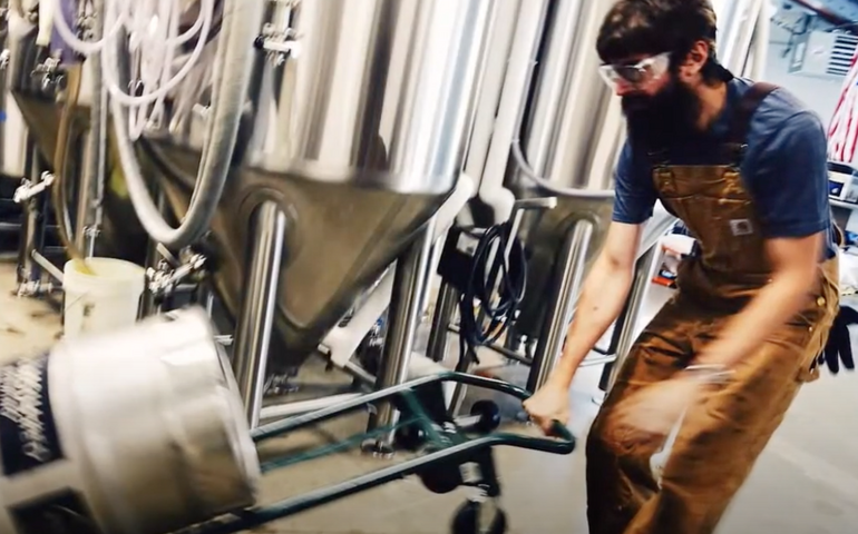screenshot of a bearded man wheeling a beer keg on a dolly