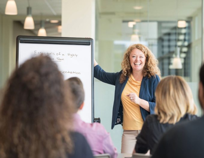 A person stands at a whiteboard with other people looking on.