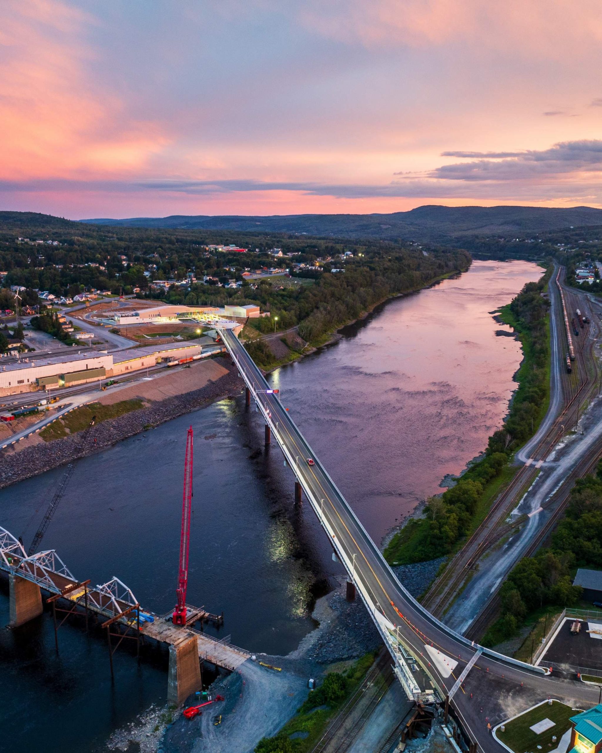 An aerial view of a bridge over a river in the pink sunlight.