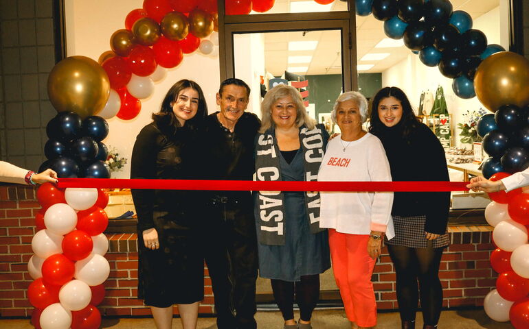 Five people stand with a ribbon and balloons.
