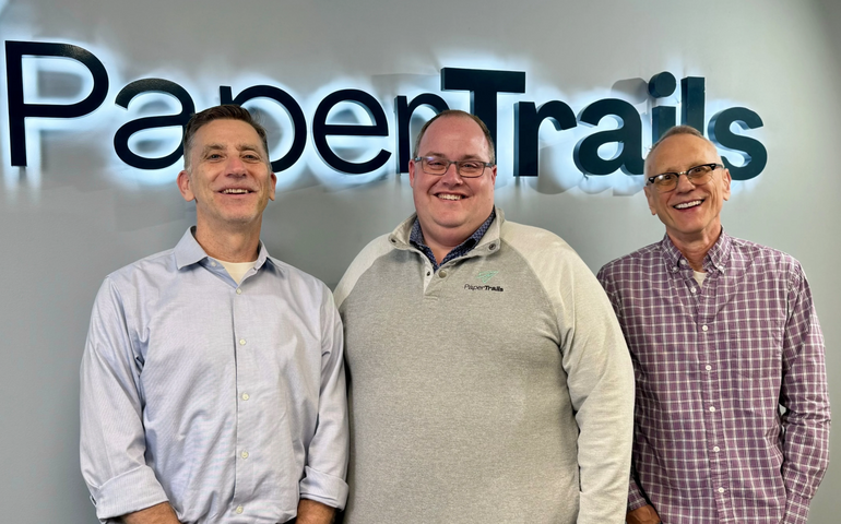 Three people pose in front of a sign.