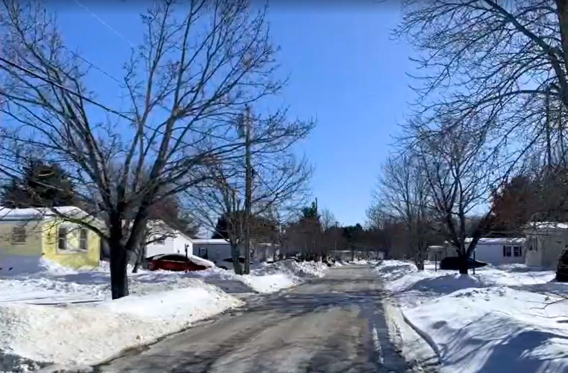 A road has homes and snowy lawns.