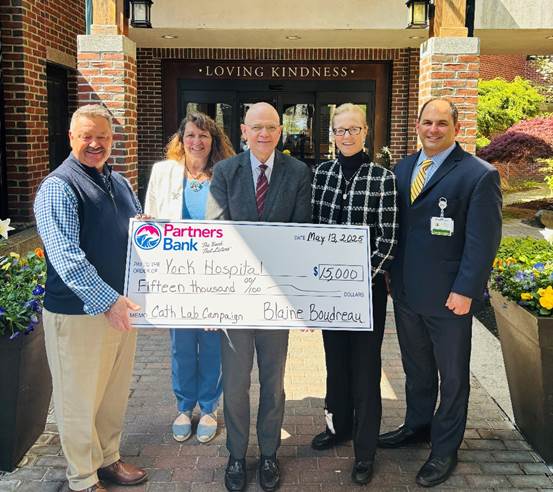 Five people pose with an oversize check outside a bulidng.