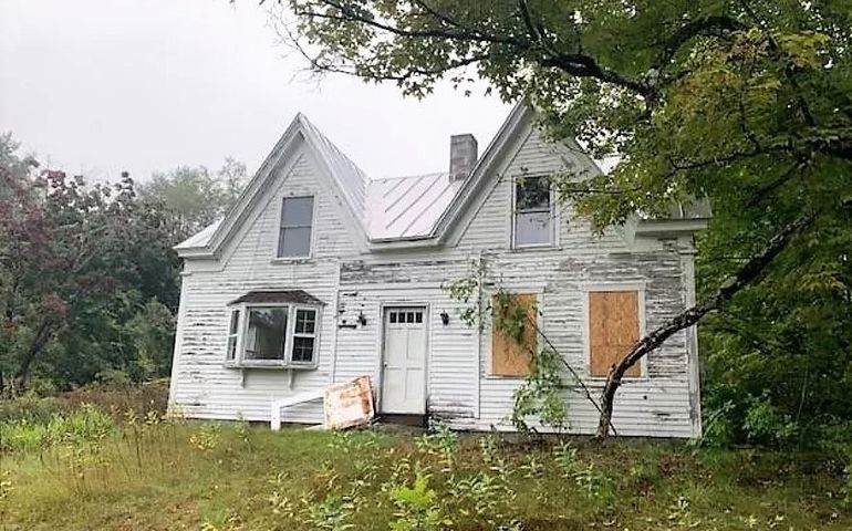 white farmhouse with peeling paint and boarded windows
