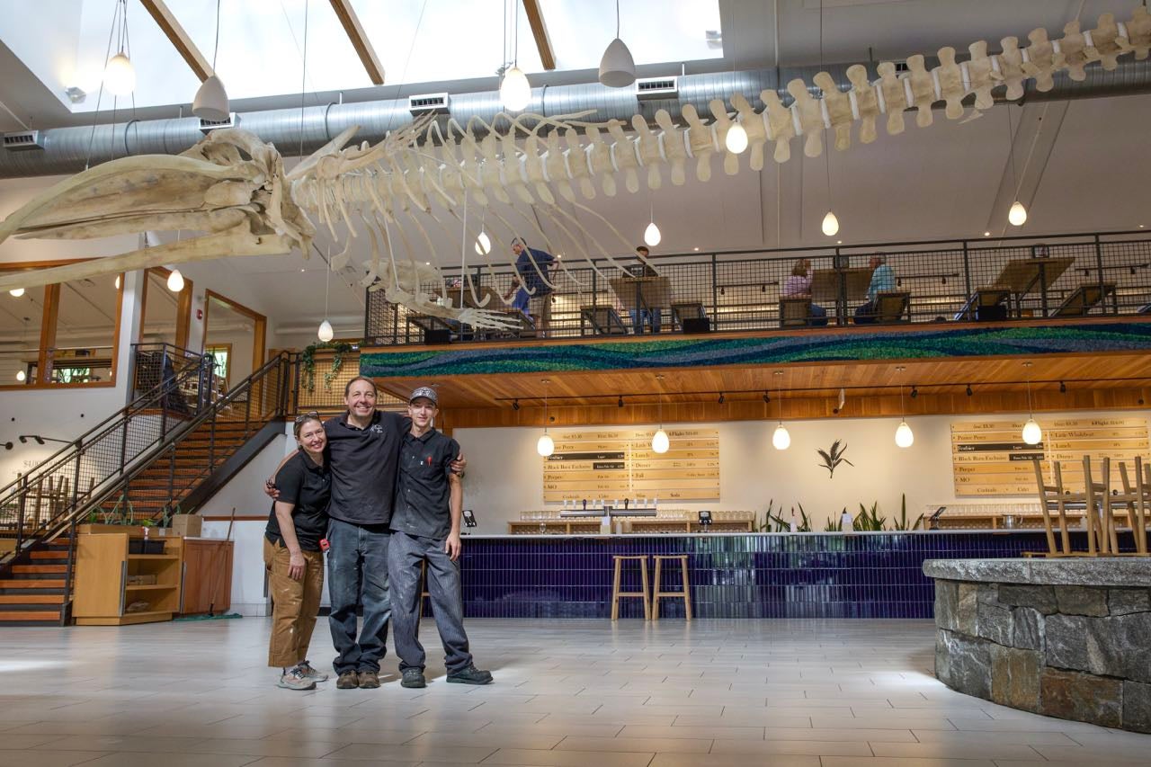 Three people stand below a skeleton.