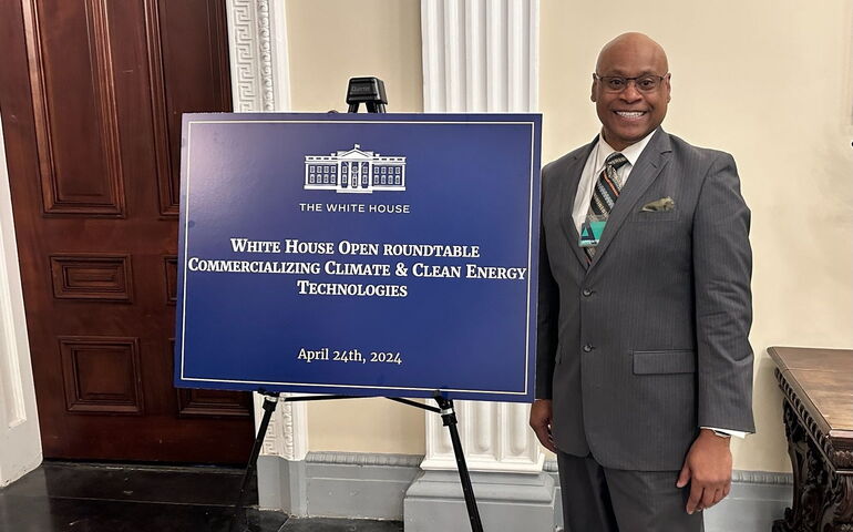 Brien Walton of Husson University stands in the White  House next to a sign.