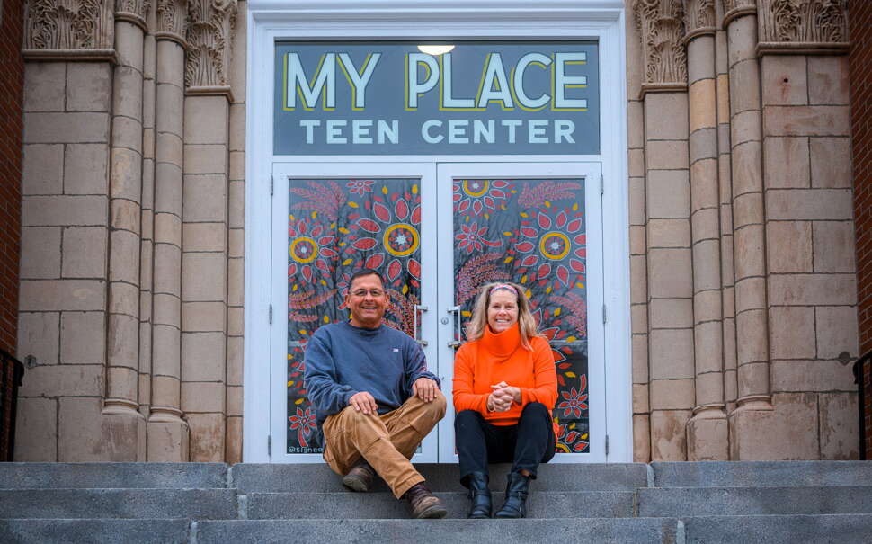 Two people sit on the steps of a stone building.