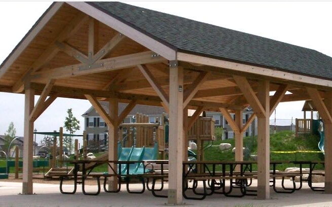 A wood-framed strucutre shades some picnic tables.
