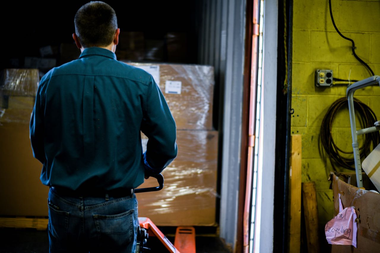 A person maneuvers a handcars with plastic-wrapped cartons.
