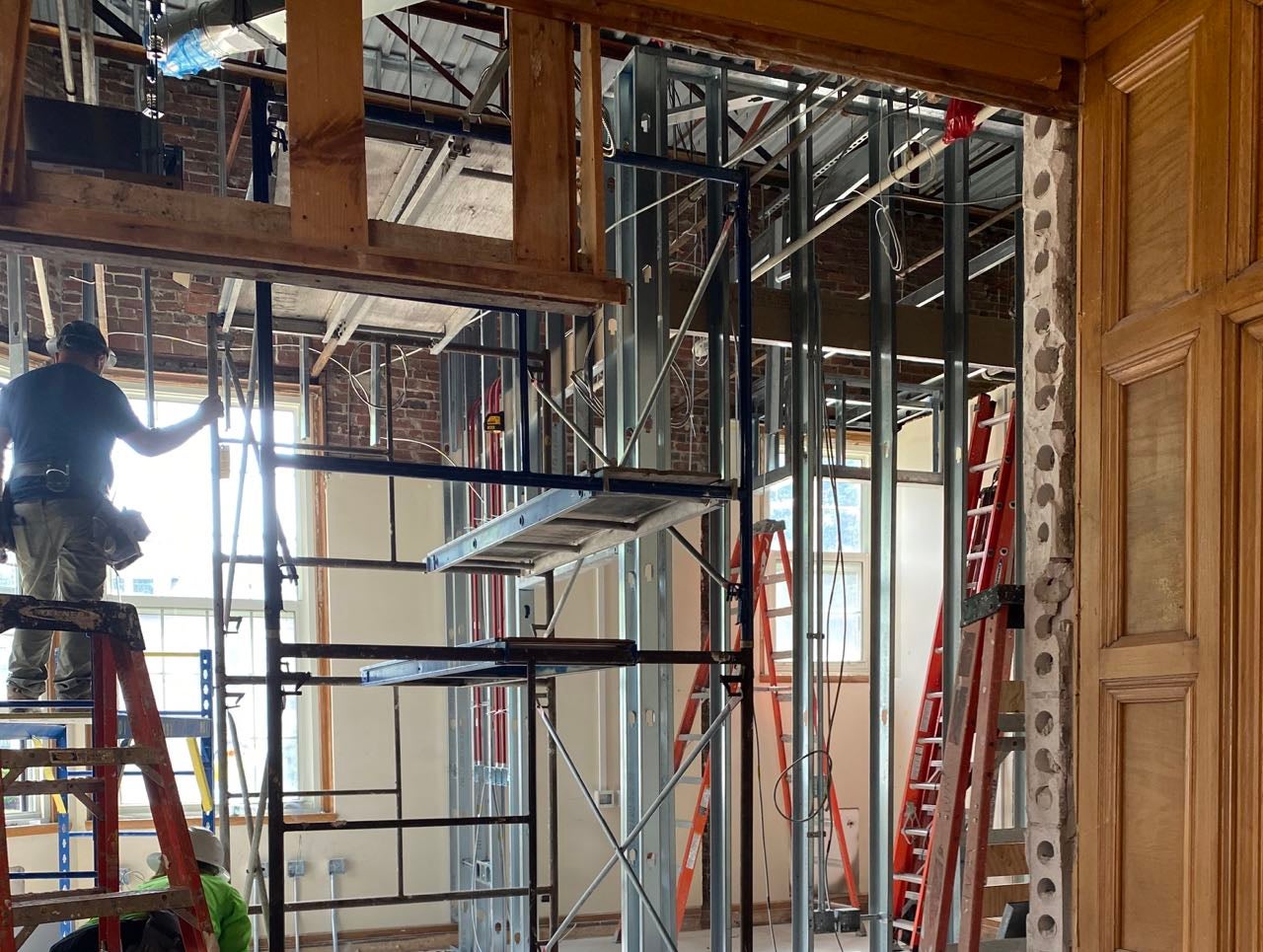 Scaffolding and a man on a ladder are inside a room.